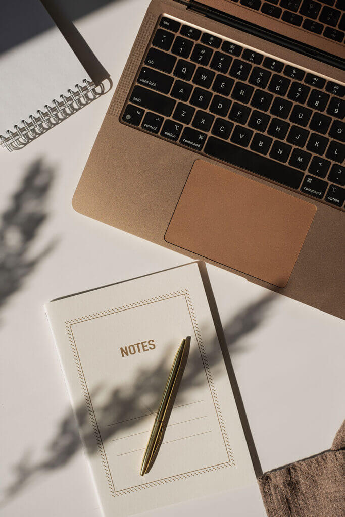 Overhead view of a laptop, notebook labeled 'NOTES', and a pen, representing adult counseling sessions and reflection.